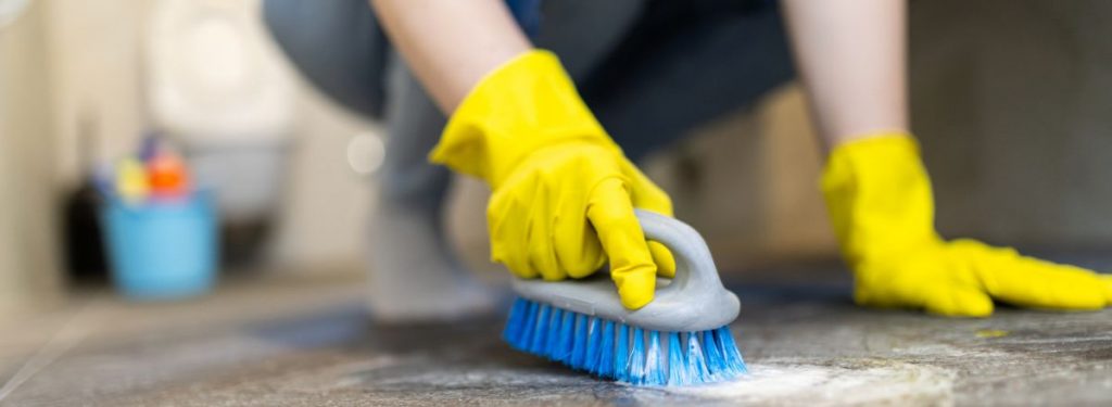 A cleaner wearing gloves scrubbing a wet floor with a brush