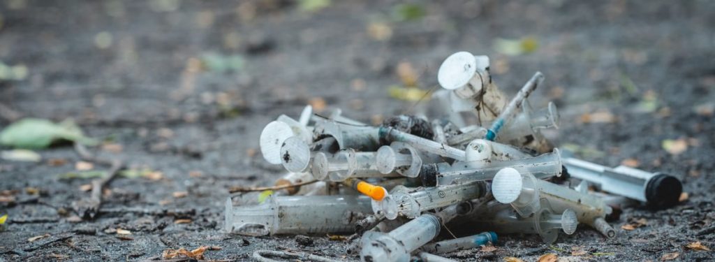 Discarded syringes and needles in a clump on the ground