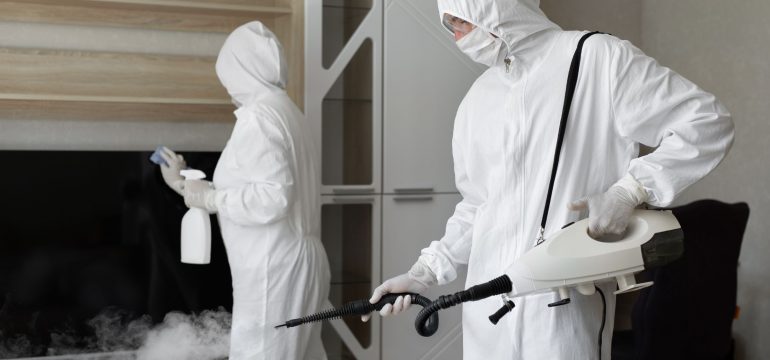 Specialist biohazard remediation team in full Category 3 PPE decontaminating a fouled area indoors