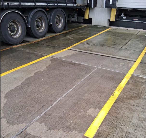 Cleaned concrete loading dock pavement showing only a faint damp mark where a large oil spill was removed, next to a semi-truck.